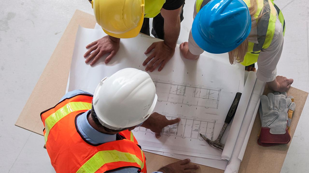 construction workers wearing hardhats examining blueprints on a table