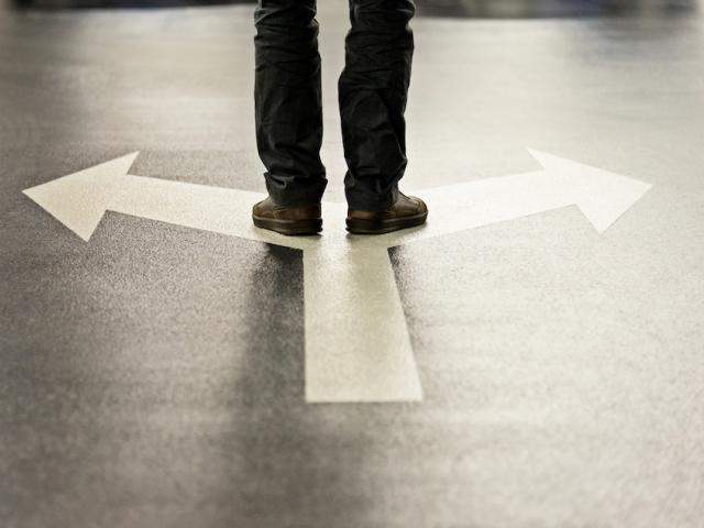 Pair of feet standing on arrows painted on the ground that point left and right